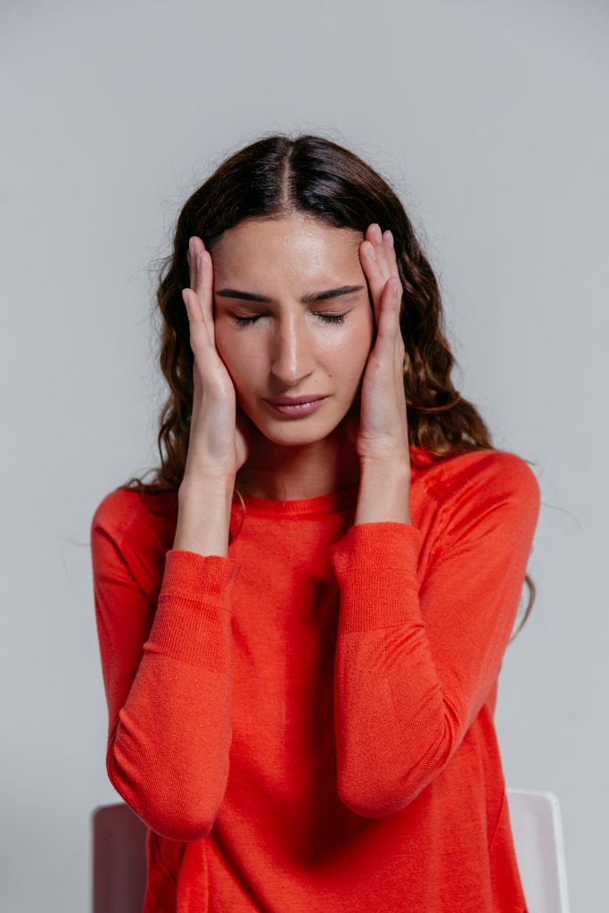 A young woman in a red sweater holding her head, depicting stress or headache.